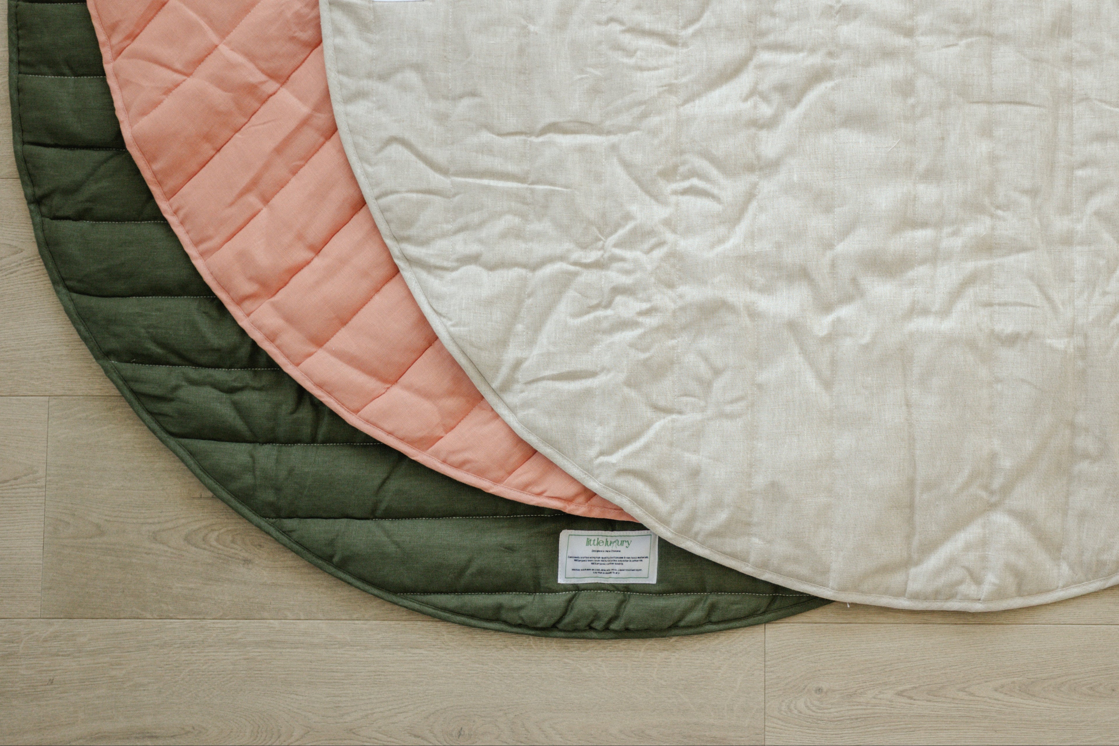 Three round quilted mats in green, pink, and beige on a wooden floor.