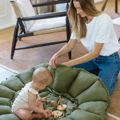Woman and baby playing on a green cushioned mat in a home setting